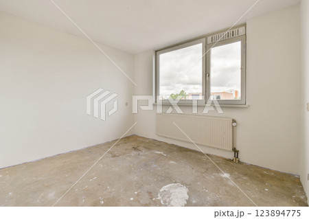 A spacious, uncluttered room featuring white walls and a large window, allowing natural light to flood in. The floor is bare, showcasing a minimalist aesthetic. 123894775