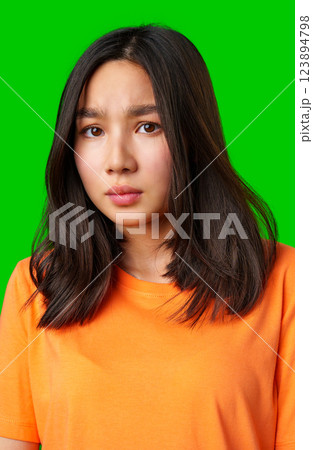 Young woman with long dark hair in orange shirt expresses curiosity against a bright green background Young woman with long dark hair in orange shirt expresses curiosity against a bright green background 123894798
