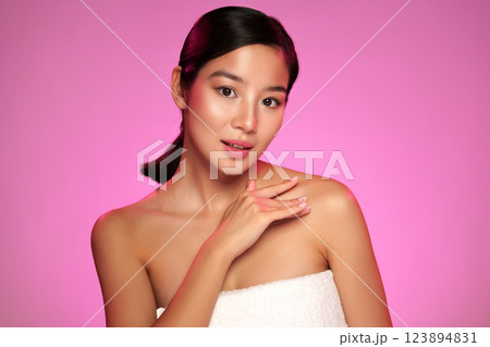 Woman with natural makeup poses gracefully against a pink background while displaying skincare routine Woman with natural makeup poses gracefully against a pink background while displaying skincare routine 123894831