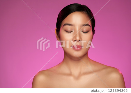 Young woman with closed eyes in front of a vibrant pink background captures a serene moment of relaxation and self-care 123894863