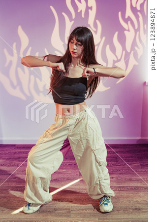 Young woman dances confidently in casual clothing with unique lighting and background patterns Young woman dances confidently in casual clothing with unique lighting and background patterns 123894871