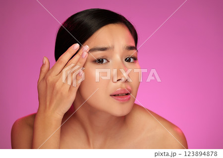 Young woman applying skincare product on her face in front of a vibrant pink background Young woman applying skincare product on her face in front of a vibrant pink background 123894878