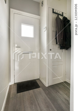 A clean and contemporary entryway showcasing a white door, simple flooring, and organized space. The minimalist aesthetic defines the ambiance. 123894906