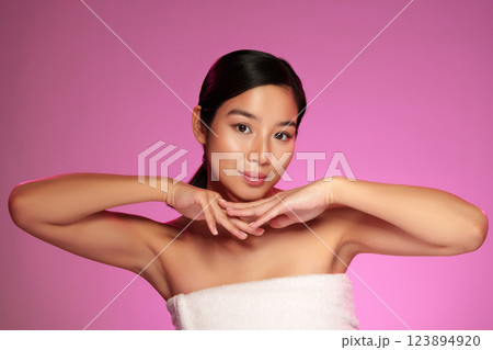 Confident young woman posing with hands under chin in front of pink background during a beauty shoot Confident young woman posing with hands under chin in front of pink background during a beauty shoot 123894920