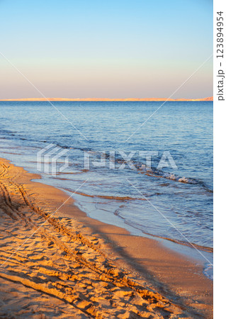 Tranquil beach landscape at sunset with gentle waves lapping on the sandy shore 123894954