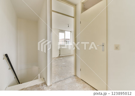 A minimalist interior space features an open door that leads to a staircase, showcasing bright white walls and a sense of openness. 123895012