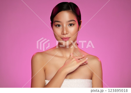Young woman with long dark hair poses against a pink background showcasing beauty and confidence in a minimalist style 123895018