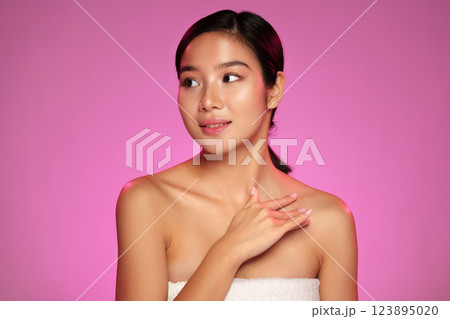 Woman displaying skincare routine with soft expression against pink background during a beauty tutorial session Woman displaying skincare routine with soft expression against pink background during a beauty tutorial session 123895020