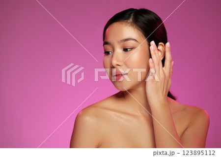 Woman posing with hand on face against a vibrant pink background during a beauty photoshoot Woman posing with hand on face against a vibrant pink background during a beauty photoshoot 123895112