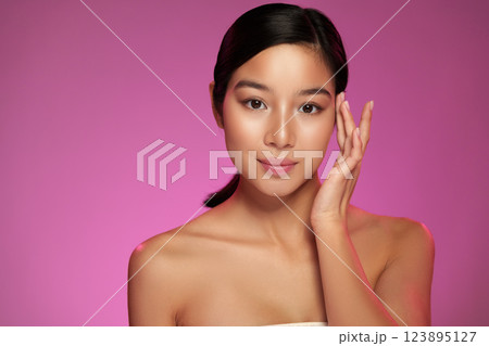 Woman with smooth skin touching her face against a pink background during a beauty shoot 123895127