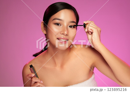Model applies mascara in a beauty shoot with vibrant pink background showcasing makeup techniques Model applies mascara in a beauty shoot with vibrant pink background showcasing makeup techniques 123895216