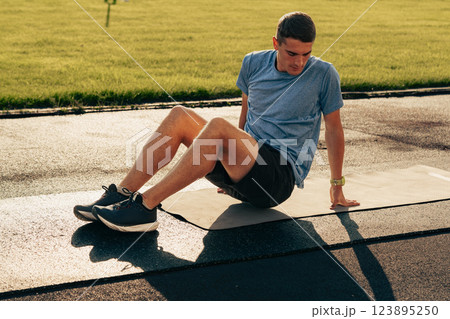 Young man performs bodyweight exercises on mat in park during sunny afternoon workout session 123895250