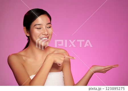 Smiling woman posing with outstretched hand against a vibrant pink background 123895275