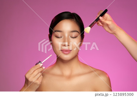 Makeup application process on a smiling woman with a bright background featuring hands and beauty products 123895300