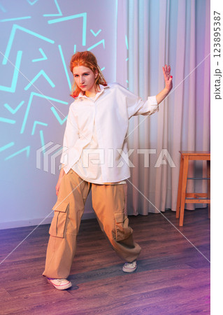 Dynamic dance performance by a young woman in casual attire in a vibrant indoor setting with colorful lighting 123895387