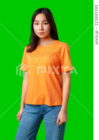 Young woman posing in bright orange t-shirt against green backdrop in a studio setting 123895393