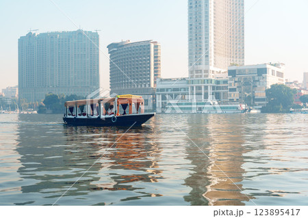 Boaters enjoying a calm morning on the river beside modern buildings in a bustling city Boaters enjoying a calm morning on the river beside modern buildings in a bustling city 123895417
