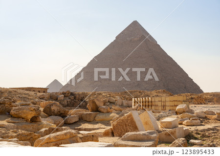 Pyramids of Giza stand majestically under clear skies with ancient ruins nearby at midday 123895433