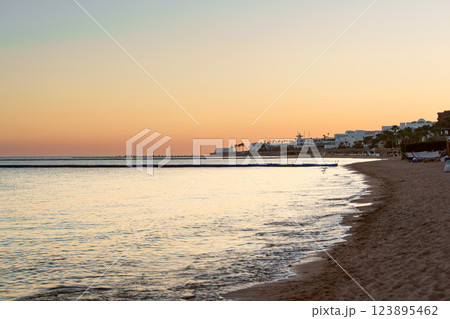 Tranquil beach at sunset reflecting warm colors over calm waters near coastal town Tranquil beach at sunset reflecting warm colors over calm waters near coastal town 123895462