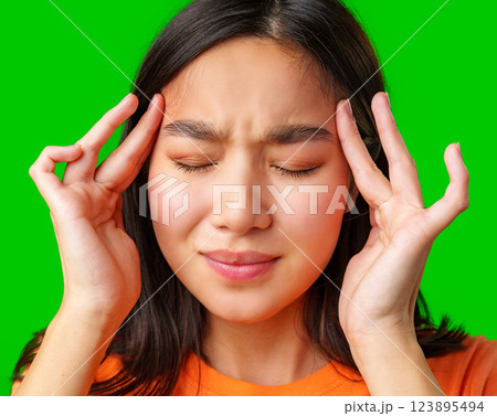 Young girl experiences headache while touching her temples in front of bright green backdrop 123895494