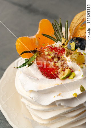 Sweet meringue dessert topped with fresh fruit and nuts on a white plate Sweet meringue dessert topped with fresh fruit and nuts on a white plate 123895516