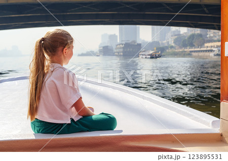 Girl enjoys a peaceful boat ride on a river surrounded by cityscape during the morning 123895531