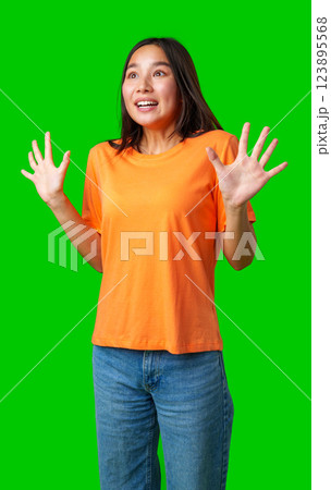 Excited young woman expresses joy and surprise against a vibrant green background during a fun moment 123895568