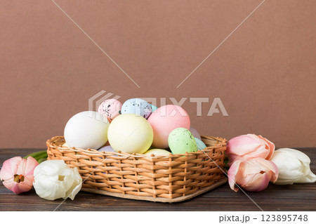Happy Easter composition. Easter eggs in basket on colored table with yellow Tulips. Natural dyed colorful eggs background with copy space 123895748