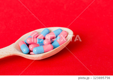 Vitamin capsules in a spoon on a colored background. Pills served as a healthy meal. Red soft gel vitamin supplement capsules on spoon 123895756