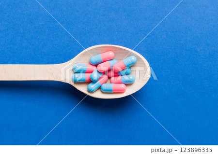 Vitamin capsules in a spoon on a colored background. Pills served as a healthy meal. Red soft gel vitamin supplement capsules on spoon 123896335