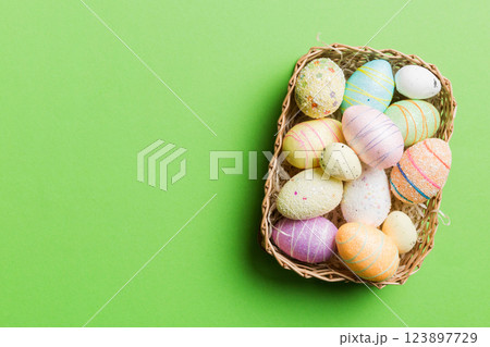 Colorful Easter eggs in wicker basket against colored background, closeup. top view with copy space Colorful Easter eggs in wicker basket against colored background, closeup. top view with copy space 123897729