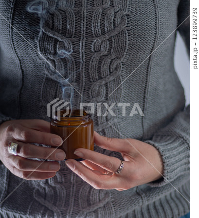 Hold a soy candle in hands. Candle in a glass jar. Cozy knitted sweater Hold a soy candle in hands. Candle in a glass jar. Cozy knitted sweater 123899739