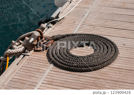 Coiled black rope on wooden dock near water with rusty metal cleats Coiled black rope on wooden dock near water with rusty metal cleats 123900428
