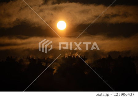 Dramatic sunset with rising chimney smoke over silhouetted village rooftops 123900437