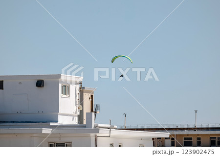 Paraglider mid-flight against clear blue sky in city 123902475