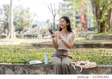 Sustainable lifestyle. Cheerful young woman smiling while using her smartphone outdoors. Sustainable lifestyle. Cheerful young woman smiling while using her smartphone outdoors. 123902802