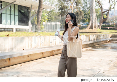 Sustainable lifestyle in motion. Young woman walking with a phone and water bottle, embracing a sustainable lifestyle. 123902815
