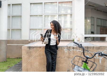 Digital Communication and Urban Greenery. A woman checks her messages while leaning against a wall with her bicycle by her side. 123902892