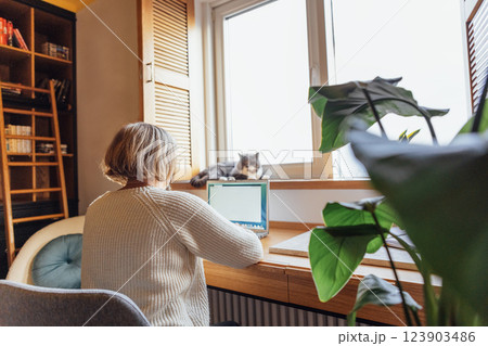 An elderly woman in casual clothes is working on a laptop. A mature lady is typing on a computer 123903486