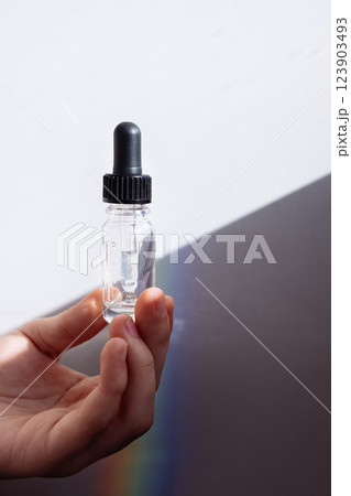 A close-up of a male hand with a transparent bottle of moisturizing serum for the face. A young man holds a cosmetic product in bright sunlight. 123903493