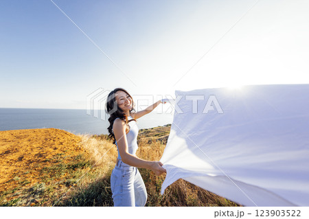 An attractive Asian woman laughs and holds an open sheet outdoors. A charming Korean woman enjoys nature. An attractive Asian woman laughs and holds an open sheet outdoors. A charming Korean woman enjoys nature. 123903522