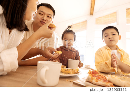 A happy Asian family is eating pizza in the kitchen at home. A young Korean couple and their cute children are having lunch. A happy Asian family is eating pizza in the kitchen at home. A young Korean couple and their cute children are having lunch. 123903531