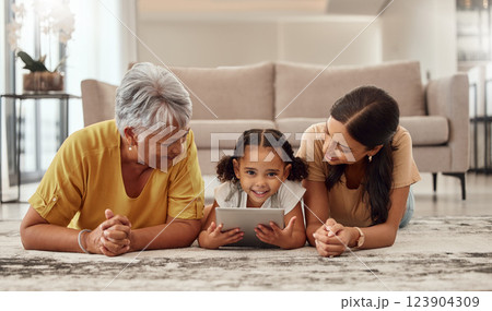 Tablet, children and family with a girl, mother and grandmother streaming or watching movies online together. Kids, internet and love with a woman, parent and daughter bonding while lying on a floor 123904309