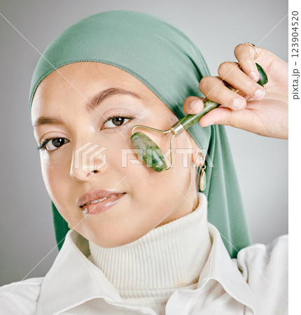 Muslim arab woman beauty, jade roller and facial skincare, cosmetics product and aesthetic wellness on studio background. Portrait islamic hijab, model face and green stone massage, self care or glow 123904520