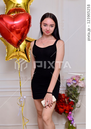 vertical photo stunning girl with long black hair poses gracefully in a black dress, with heart-shaped balloon. image exudes romance, elegance, perfect for themes of love, beauty, and celebration 123905258