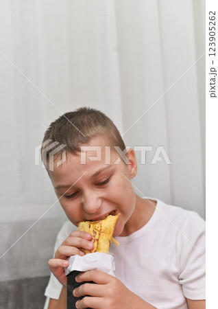 vertical photo young boy eats a delicious shawarma with gusto, his expression full of satisfaction. pleasure of enjoying flavorful food, for themes related to eating, happiness, and culinary delight. vertical photo young boy eats a delicious shawarma with gusto, his expression full of satisfaction. pleasure of enjoying flavorful food, for themes related to eating, happiness, and culinary delight. 123905262
