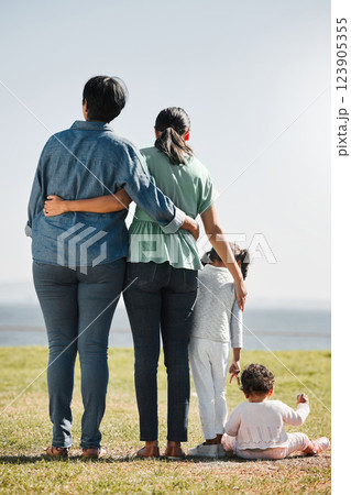 Park, nature and back view of family on grass outdoors with relatives spending quality time together. Love, support and caring grandma, mom and girl with baby bonding together with scenic ocean view. 123905355