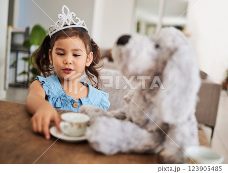 Girl, toy and tea party at a table with a princess crown, playing, having fun and talking in her home. Fantasy, creative and girl looking happy while talking to a teddy bear and drinking tea together 123905485