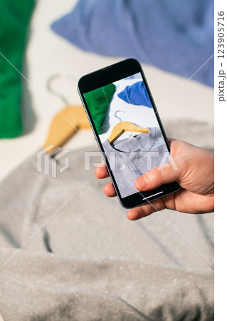 Woman hand with smartphone taking picture of used shirt. Preparing clothes to sell in second hand online shop. Resell goods and Second hand concept. Clothes donation 123905716
