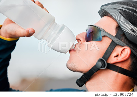 Fitness, cycling and man drinking water in bottle during a cycle marathon, training or exercise. Cardio, sports and thirsty biker athlete enjoying a refreshing drink, liquid or beverage while biking. 123905724